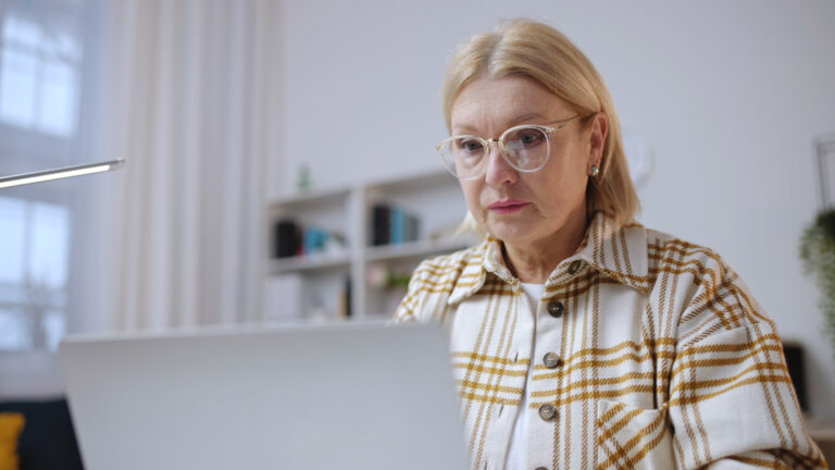 Senior woman focused on work attentively looking at laptop displ